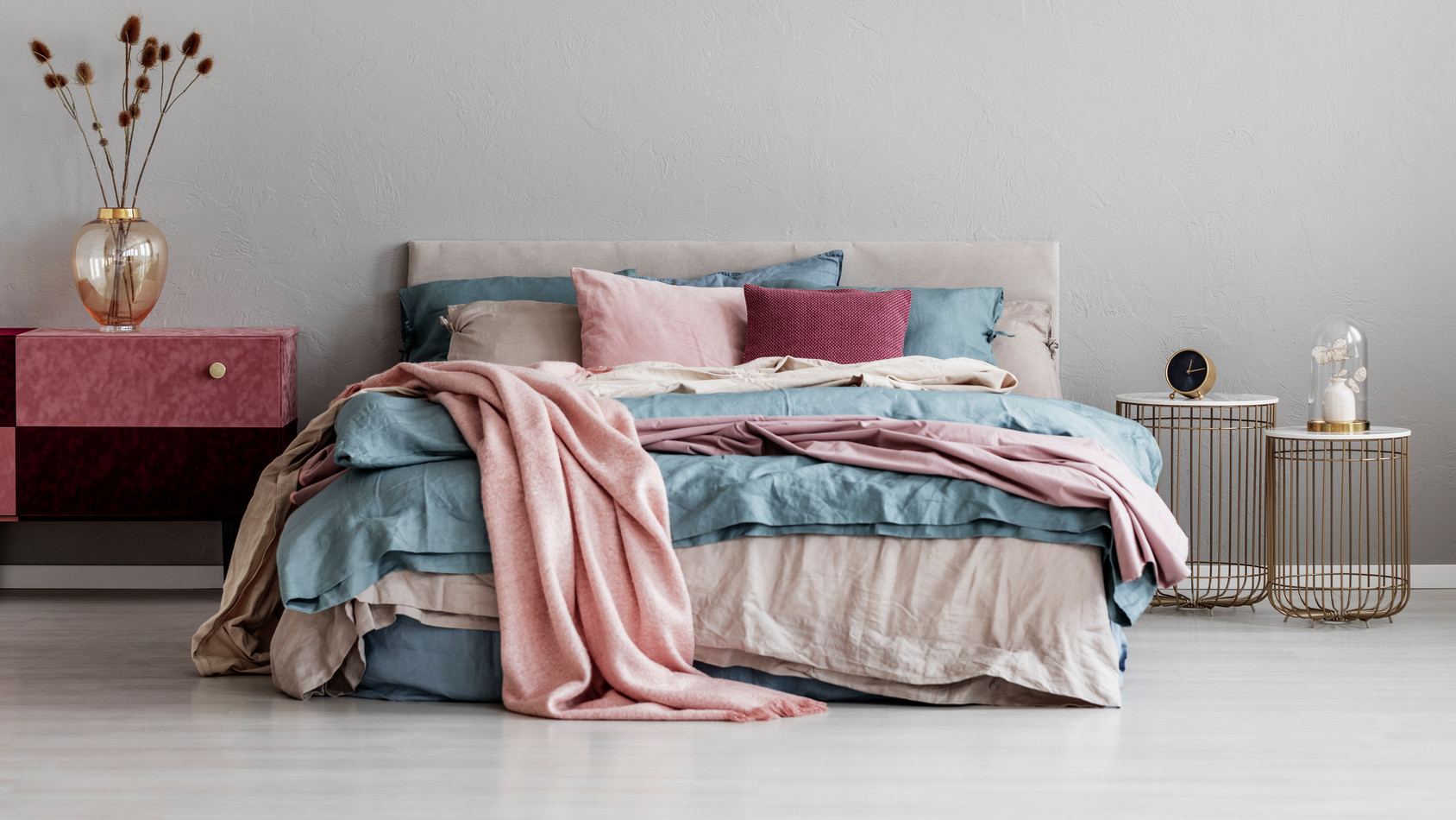 Pastel pink, beige and blue bedding on king size bed in trendy bedroom interior, copy space on empty grey wall